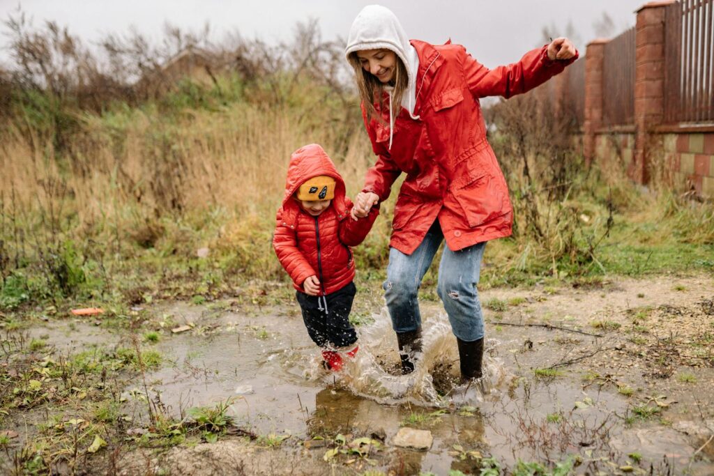 6 Brincadeiras para Dias Chuvosos Uma mulher brincando na chuva com seu filho